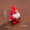 A small red and white festive Christmas dwarf figurine with a green hat and beard sitting on a wooden surface.