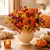 A vibrant bouquet of artificial pansy flowers in shades of orange, yellow, and deep red sits on a wooden table.