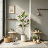 A tall artificial magnolia tree with pink silk flowers in a white pot displayed indoors.