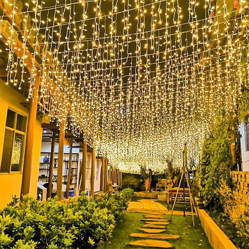 Una densa cortina de luces blancas cálidas cuelga sobre un camino de jardín y vegetación.