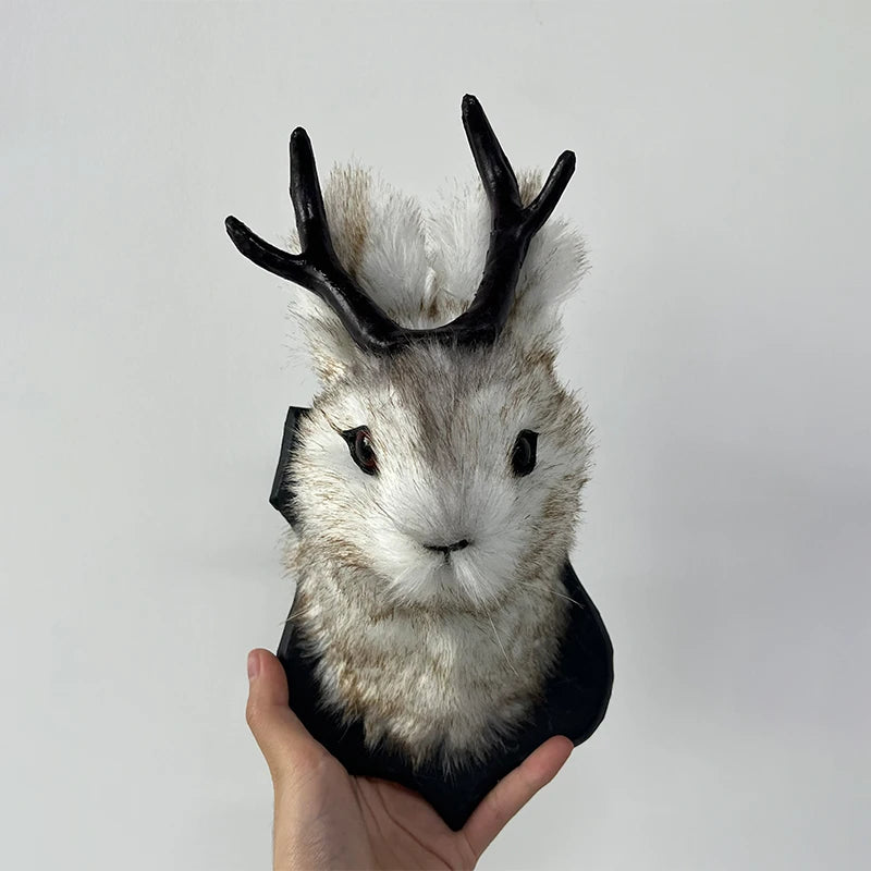 A decorative bunny head with black antlers and fluffy gray fur is held in a hand.
