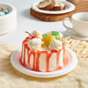 A colorful layer cake with white frosting, orange glaze, and yellow fruit garnishes sits on a white plate.