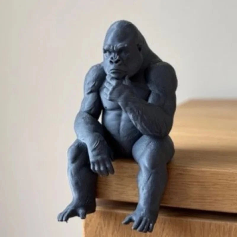 A dark gray 3D-printed figurine of a gorilla sitting and thinking, used for desk or shelf decor.