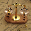 A vintage miniature balance scale with brass arms and glass pans rests on a wooden base.