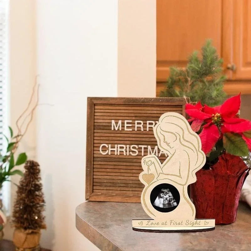 A wooden ultrasound photo frame with a silhouette of a mother and baby, set on a wooden surface.