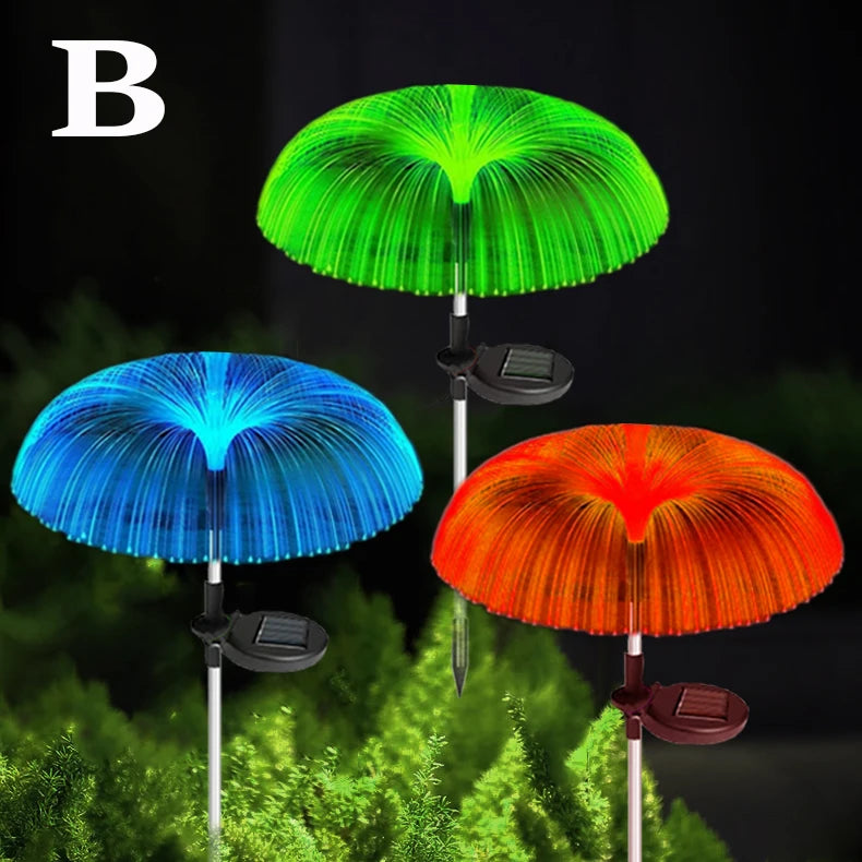 Three solar jellyfish garden lights in green, blue, and orange illuminating a green foliage background.