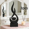 A black, three-pronged flame sculpture decor sits on a dark base in front of a white framed mirror.
