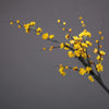 A delicate branch of artificial yellow plum blossoms against a gray background.