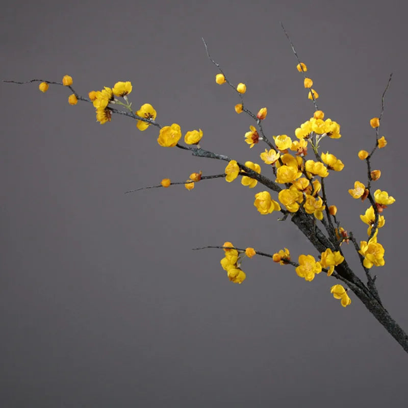 A delicate branch of artificial yellow plum blossoms against a gray background.