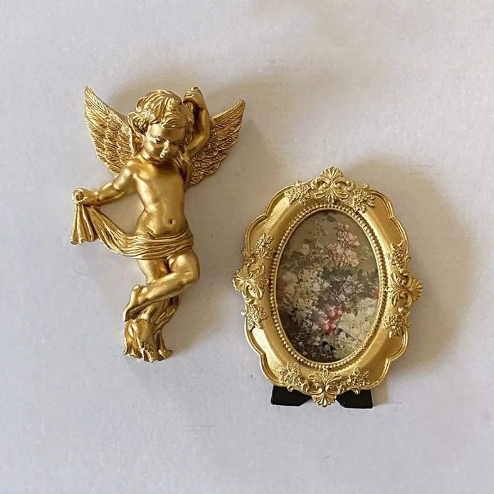 A set of gold-colored wall decor featuring a winged cherub angel statue and an ornate gold oval frame.