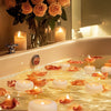 Floating candles and rose petals float on water in a bathtub with soft lighting.