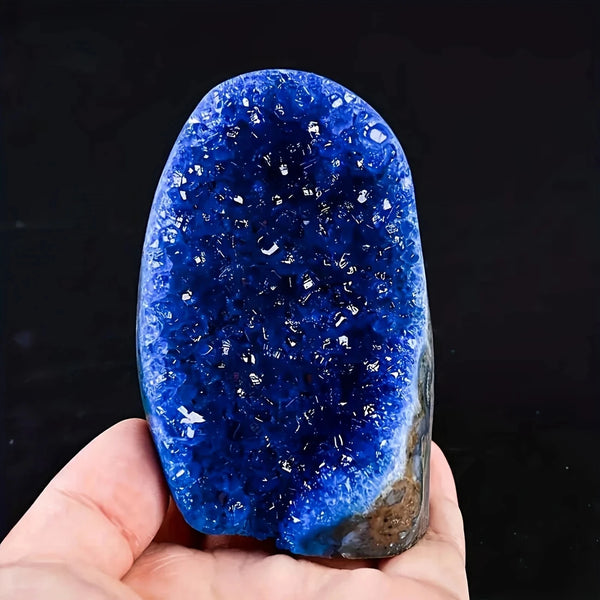 Une main tient un cluster de cristaux Bohemian Blue bleu profond et scintillant sur un fond sombre.