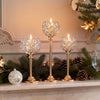 A display of elegant metal glass candle holders and pine greenery on a mantelpiece.