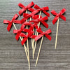 A set of red ribbon bows on wooden sticks used as cupcake toppers for parties.