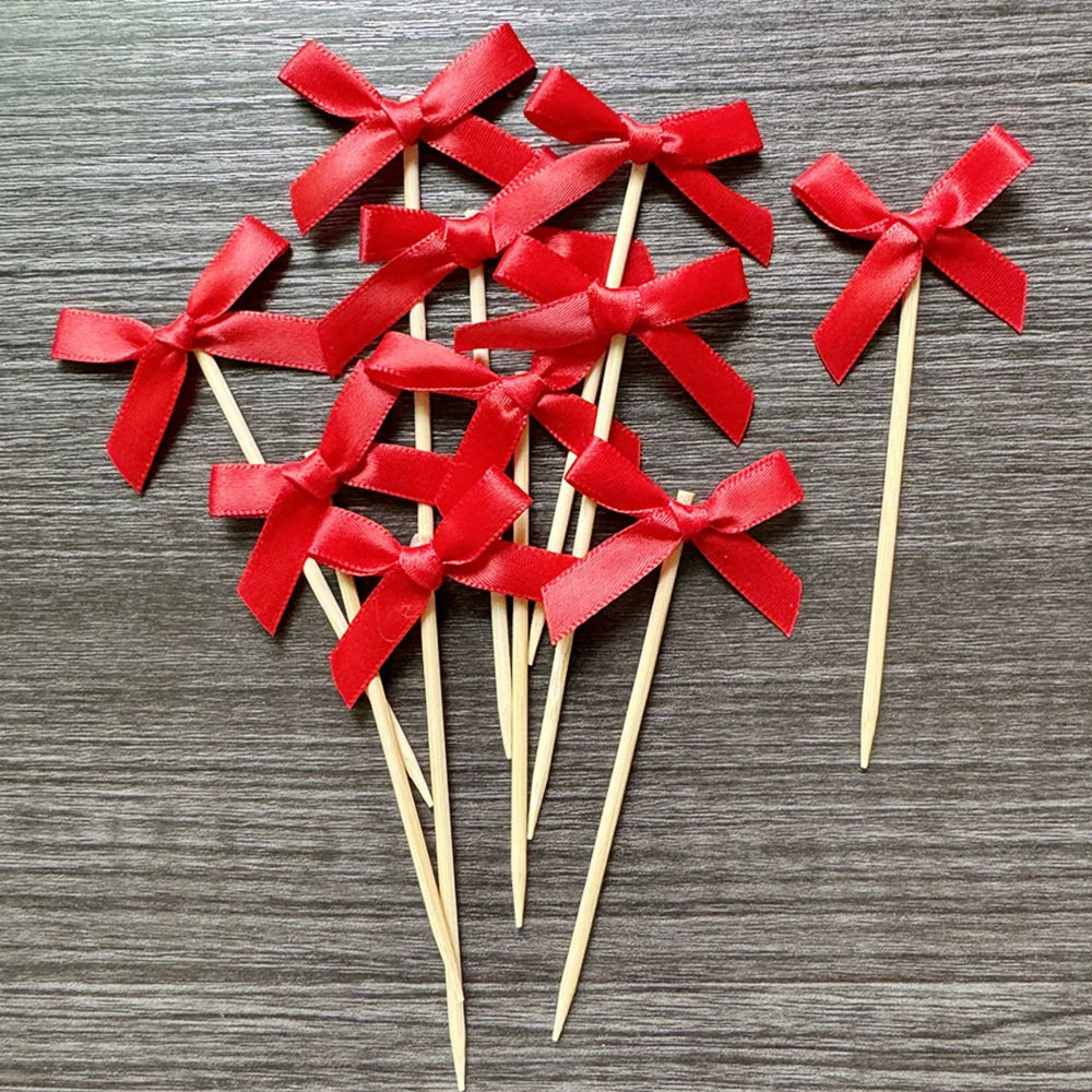 A set of red ribbon bows on wooden sticks used as cupcake toppers for parties.