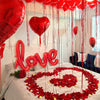 Rote herzförmige Ballons und Rosenblüten auf einem Bett für einen romantischen Anlass.
