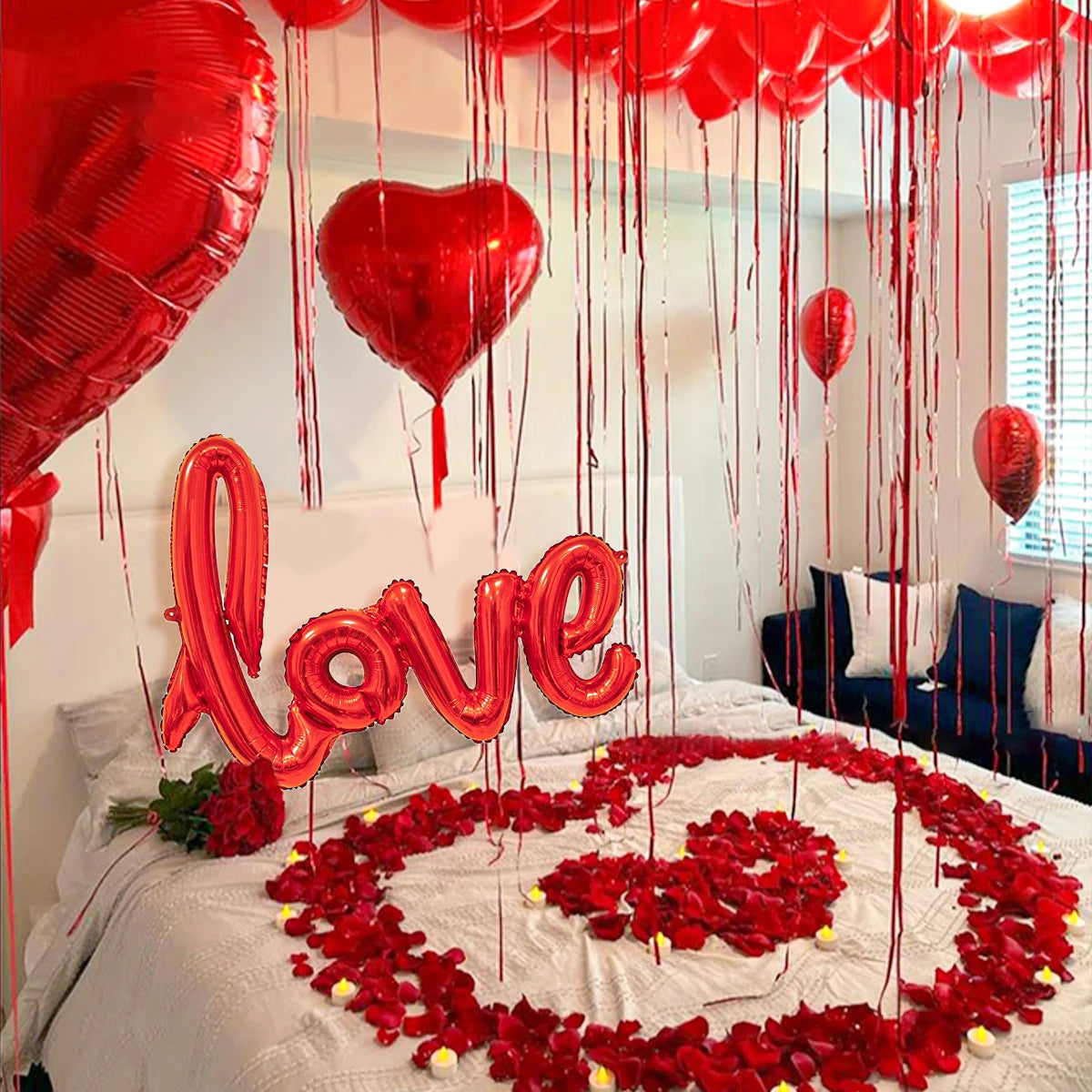 Rote herzförmige Ballons und Rosenblüten auf einem Bett für einen romantischen Anlass.