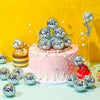 A pink cake decorated with silver disco ball ornaments and white pearls against a yellow background.