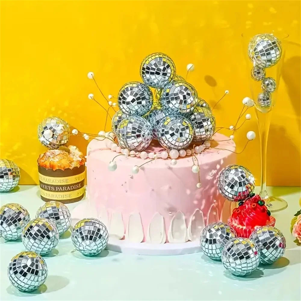 A pink cake decorated with silver disco ball ornaments and white pearls against a yellow background.