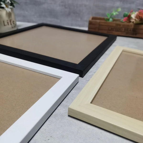 A light wood photo frame with a white border is displayed on a gray surface next to a black frame.