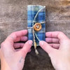 A handmade prayer quilt featuring a blue plaid fabric with a silver cross pocket shrine being held by hands.