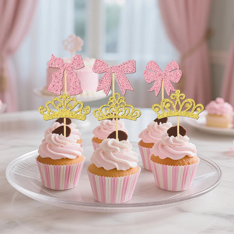 Pink and gold cupcake toppers featuring elegant crowns and bows on a white platter.