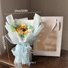 A bouquet of handmade crochet flowers in blue and yellow hues wrapped in sheer light blue fabric.