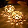 A close-up of a gold crystal tealight candle holder with a metal base casting warm light on a surface.