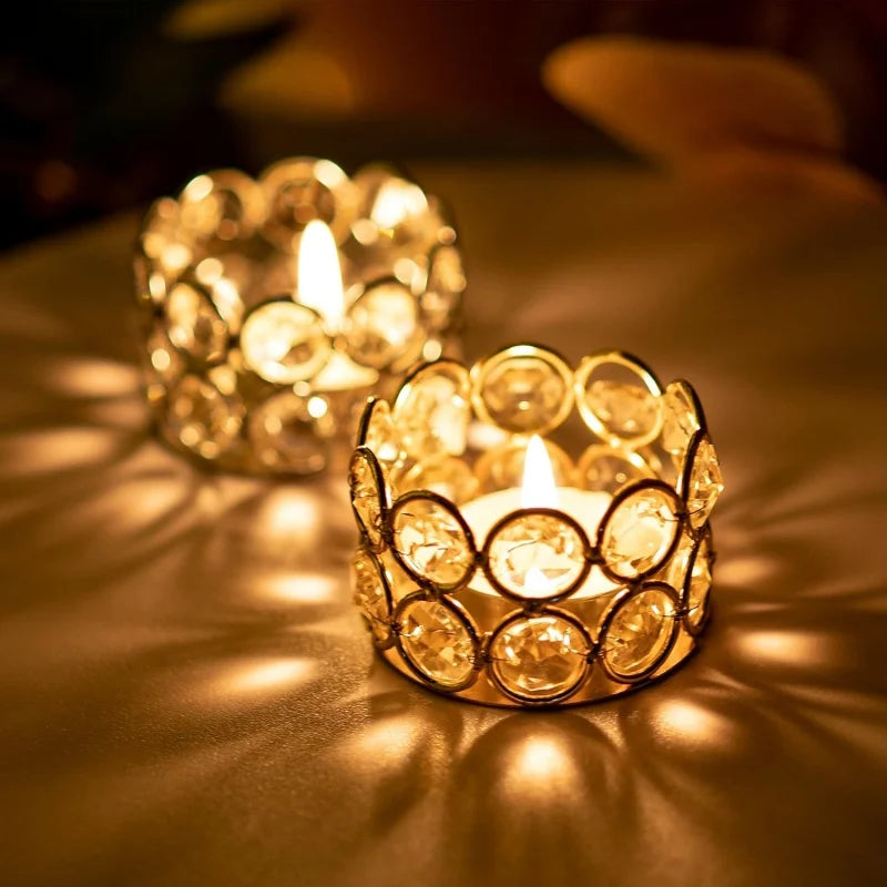 A close-up of a gold crystal tealight candle holder with a metal base casting warm light on a surface.