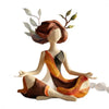 A resin sculpture of a yoga girl with brown hair and leafy antlers, wearing an orange and black outfit.