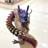 A hand holds a purple and pink articulated 3D printed dragon figurine with textured scales.