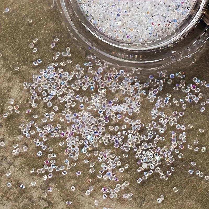 A pile of clear and iridescent multicolor glass micro beads scattered on a textured surface next to a glass container.