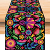 A vibrant floral pattern linen table runner featuring pink, purple, yellow, and teal flowers on a black background.