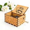 A hand-cranked wooden music box featuring an illustration of a married couple carved into the lid.