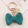 A sparkling teal rhinestone bow keychain attached to a gold split ring.