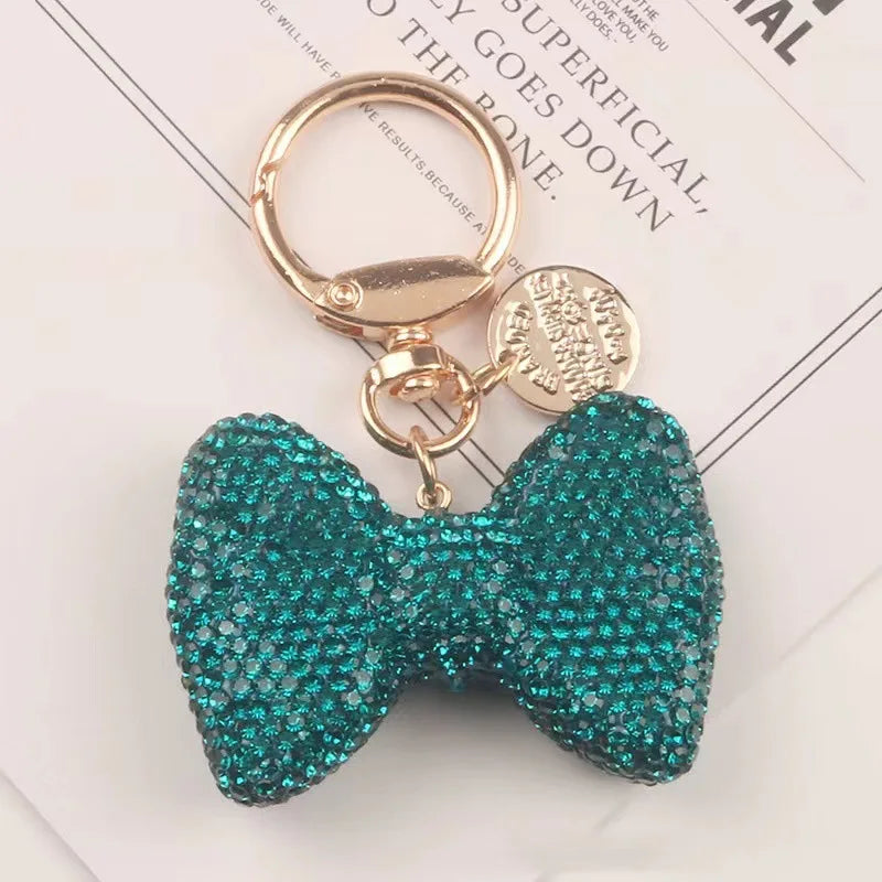 A sparkling teal rhinestone bow keychain attached to a gold split ring.