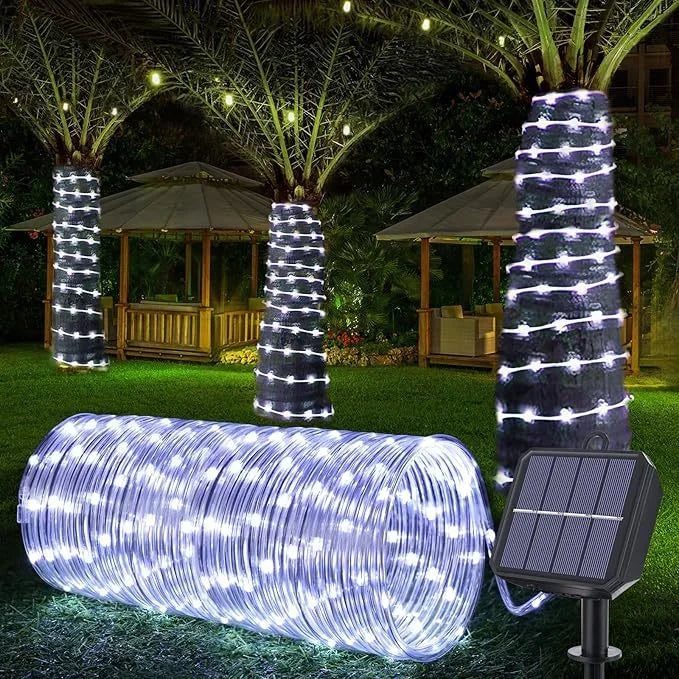 A long, cylindrical solar-powered LED rope light illuminates a garden area at night.