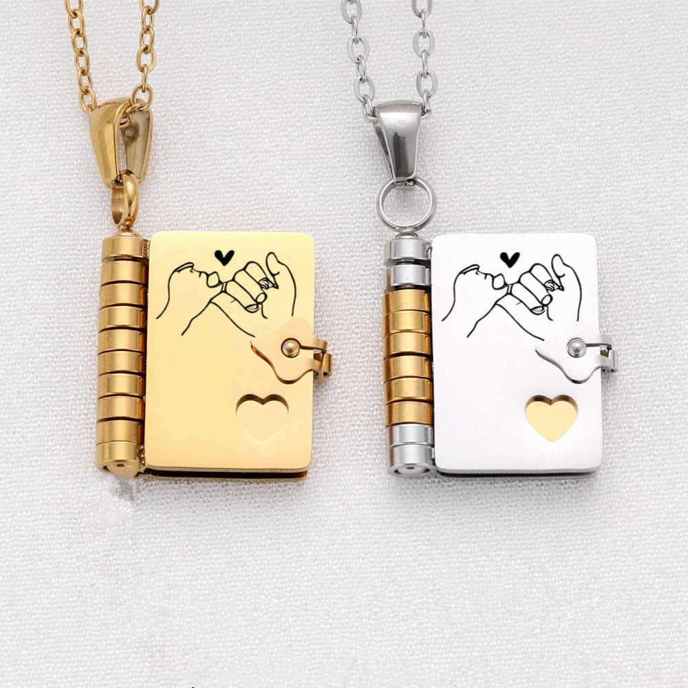 A gold-toned pendant necklace featuring an openable book charm with a handprint engraving and a silver-toned version.