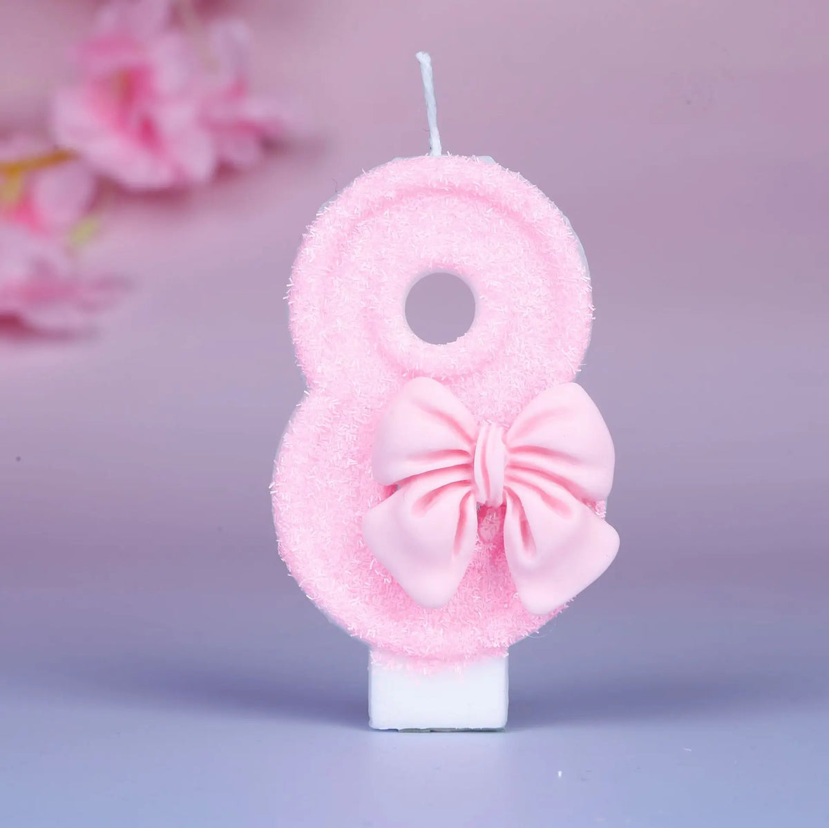 Glittery pink number eight birthday candle with a decorative bow on a white stick