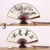 A black and white painted folding fan with a red border and Japanese calligraphy on a wooden display stand.