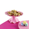 A pink plastic cake stand holding small sandwich cookies on a pink surface.