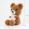 A handmade crochet teddy bear doll in brown with black eyes and white muzzle, accompanied by an inspirational card.