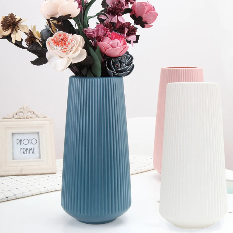 A tall, ribbed teal ceramic vase holds a bouquet of pink and burgundy flowers.