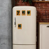 A vintage style refrigerator featuring several framed wooden magnets depicting playful black cat art.