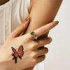 A hand wearing a gold ring with a blue gemstone and a butterfly temporary body art sticker on the wrist.