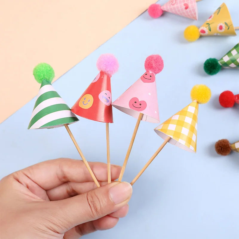 A hand holds a set of mini birthday cake toppers featuring colorful conical shapes and fuzzy pom-poms.
