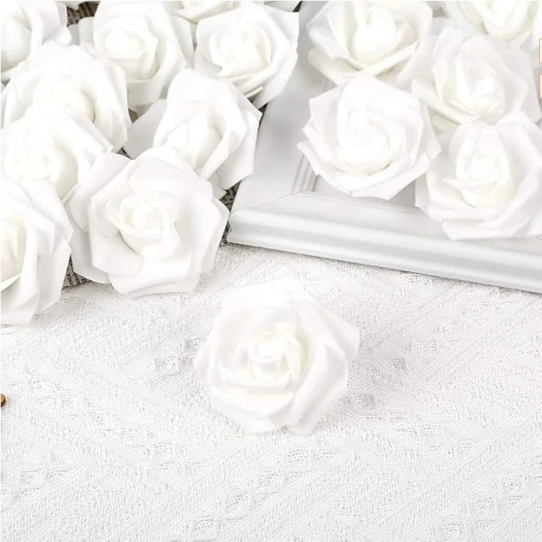 A close-up of white artificial foam rose decorations arranged in a white rectangular dish on a white textured surface.