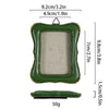 A vintage baroque resin picture frame in olive green with a gold rim and a small wooden base.
