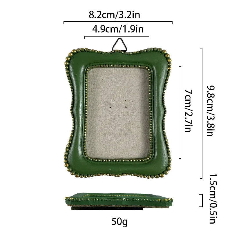 A vintage baroque resin picture frame in olive green with a gold rim and a small wooden base.