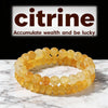 A stack of golden citrine crystal beaded bracelets displayed on a white marble surface.